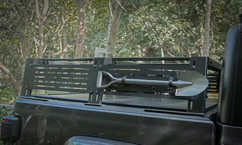 Black truck bed with a metal tool rack and shovel, set against a natural background.